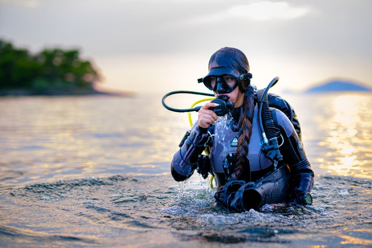 Woman diver in full gear emerging from Toroni waters during a stunning sunset.