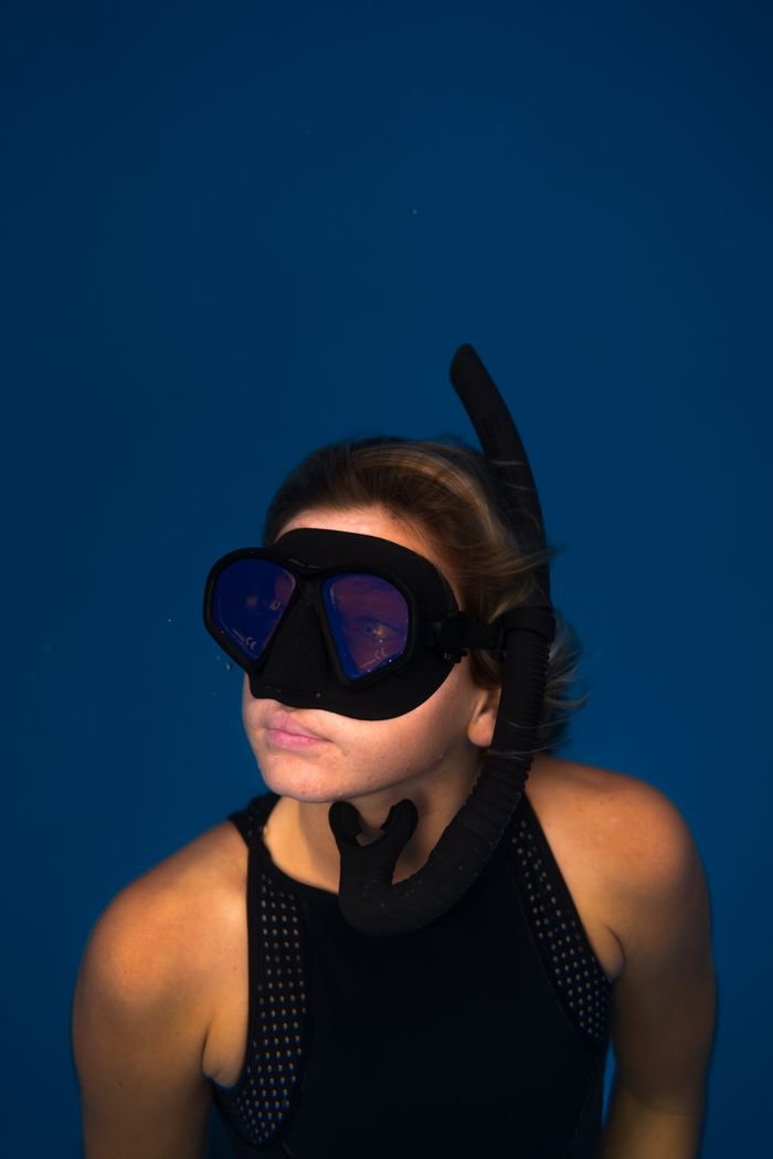 Tranquil woman in swimwear and mask diving with snorkel and looking away underwater